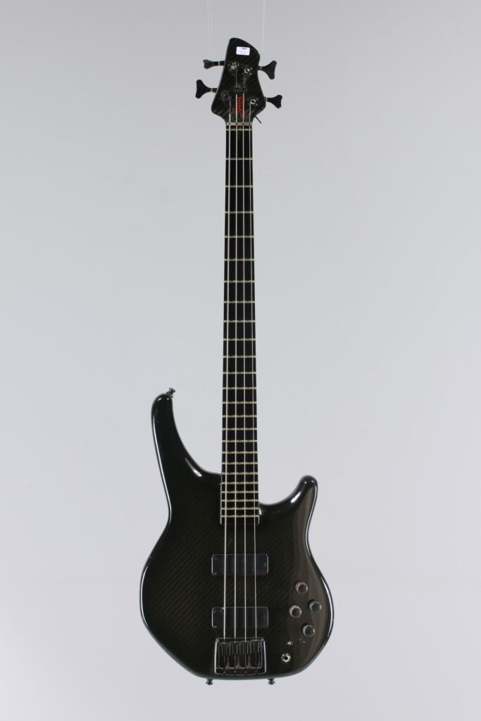 N° 117 - Guitare basse électrique solidbody STATUS, modèle Graphite Stealthe bass faite vers 1995, made in UK, finition fibre de carbone. Collection Francis Kuntz. Instrument mis en vente par Vichy Enchères le 7 novembre 2026. © Vichy Enchères / Photo C. Darbelet