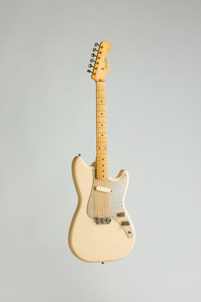 N° 130 - Guitare électrique solidbody FENDER, modèle Musicmaster, faite en 1958, made in USA, finition Desert Sand, avec un pickguard Anodisé. Collection Francis Kuntz. Instrument mis en vente par Vichy Enchères le 7 novembre 2026. © Vichy Enchères / Photo C. Darbelet